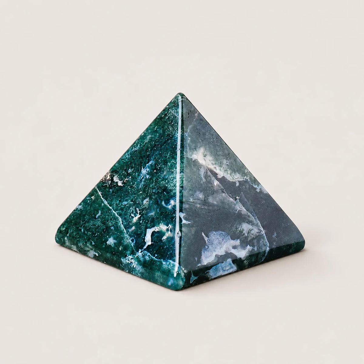Polished moss agate pyramid crystal ornament on a warm ivory background