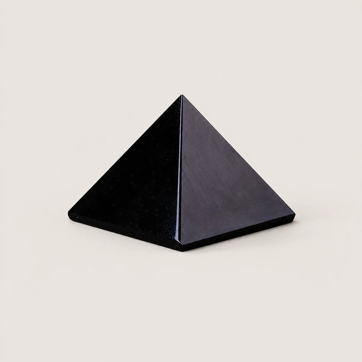 Polished obsidian pyramid crystal ornament on a warm ivory background