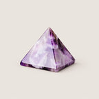 Polished amethyst pyramid crystal ornament on a warm ivory background