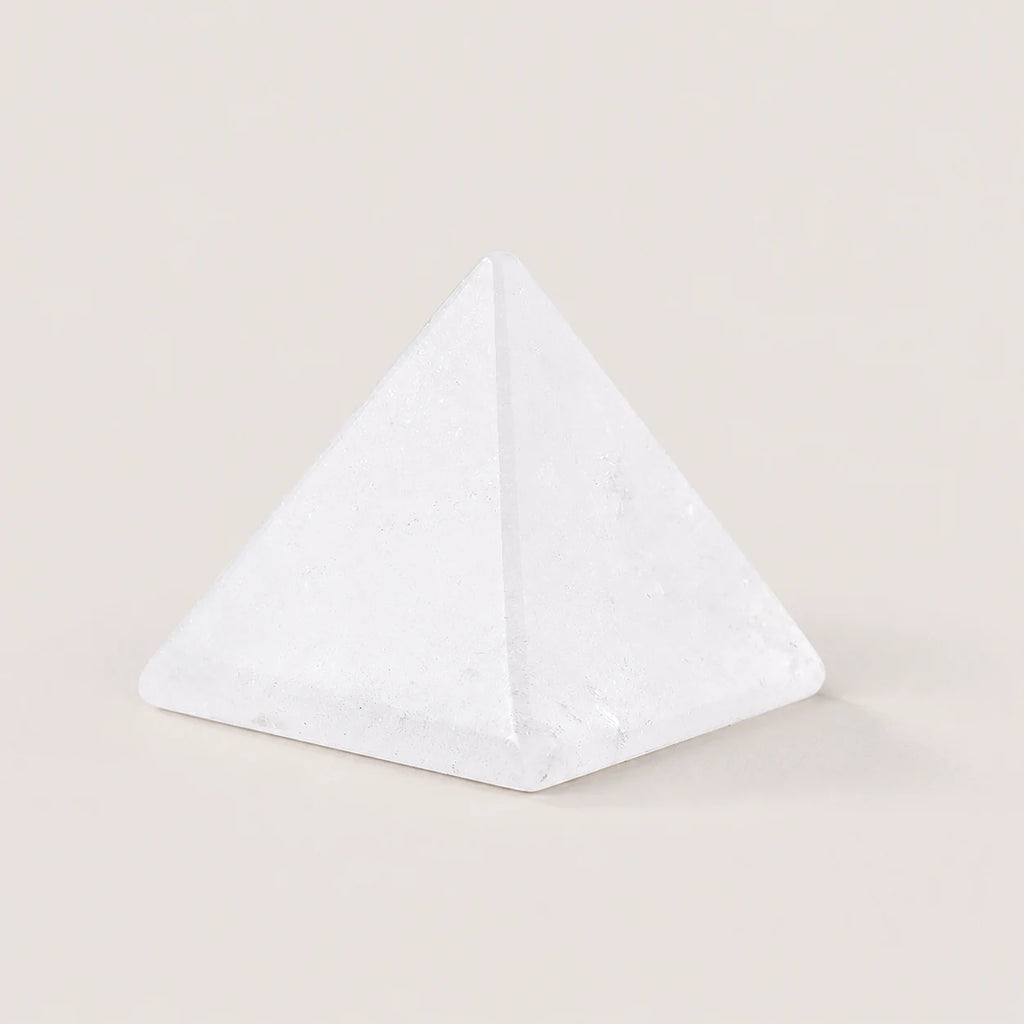Polished clear quartz pyramid crystal ornament on a warm ivory background