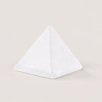 Polished clear quartz pyramid crystal ornament on a warm ivory background