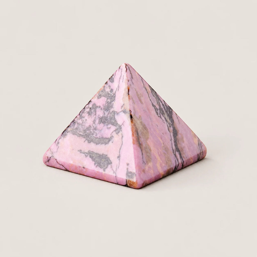 Polished rhodonite pyramid crystal ornament on a warm ivory background