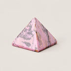 Polished rhodonite pyramid crystal ornament on a warm ivory background