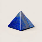 Polished lapis lazuli pyramid crystal ornament on a warm ivory background