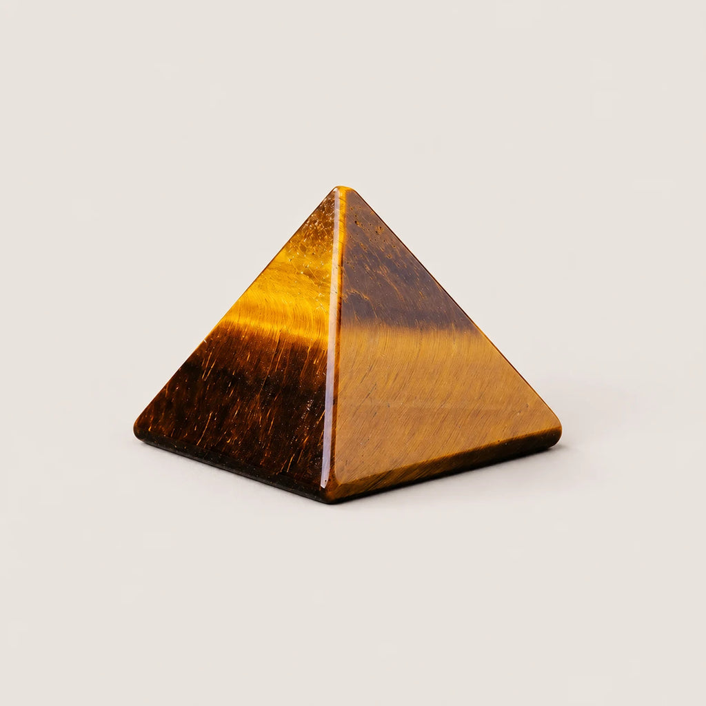Polished tiger's eye pyramid crystal ornament on a warm ivory background
