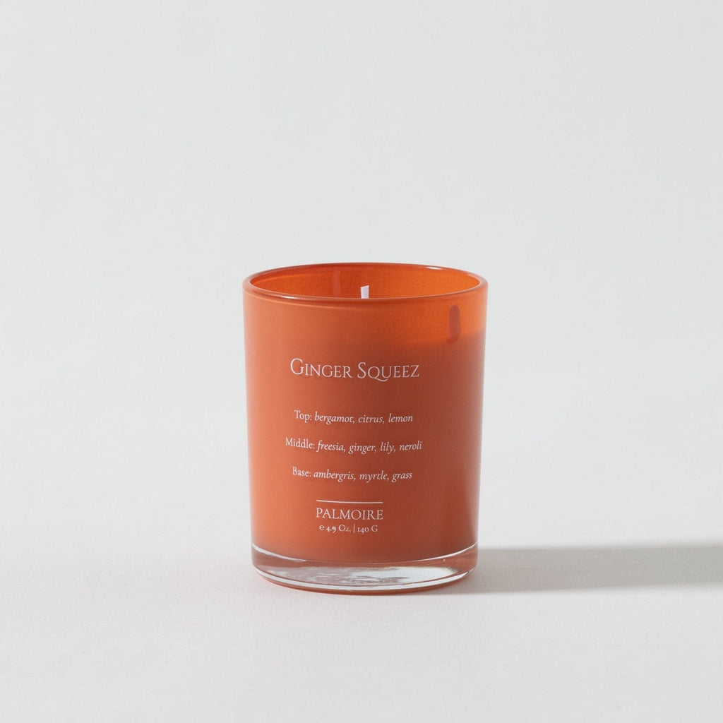 Orange glass soy wax candle with white text, labeled Ginger Squeez, lit wick visible.