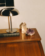 Polished wooden cabinet with a black lamp, book, quartz, and amethyst.