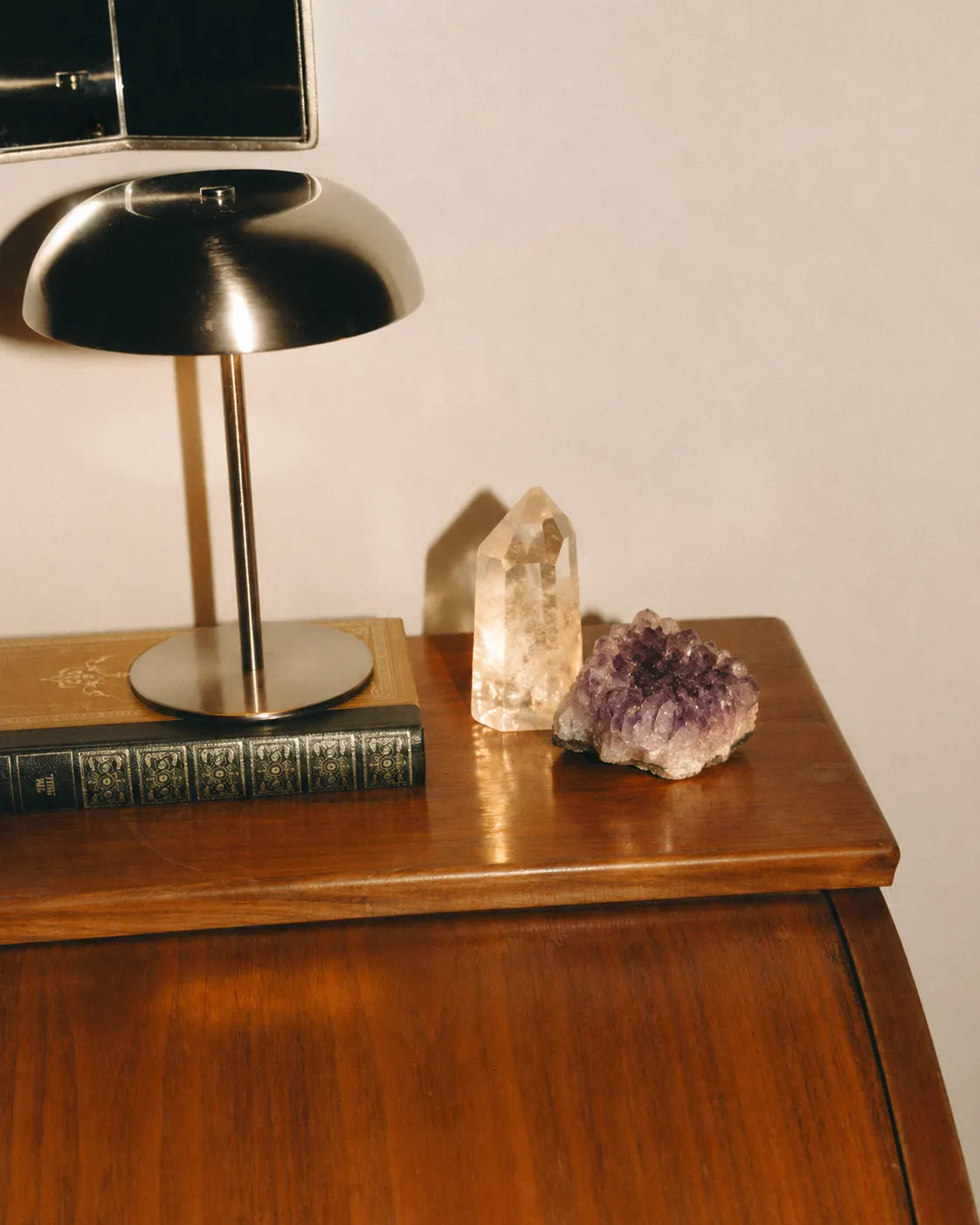 Polished wooden cabinet with a black lamp, book, quartz, and amethyst.