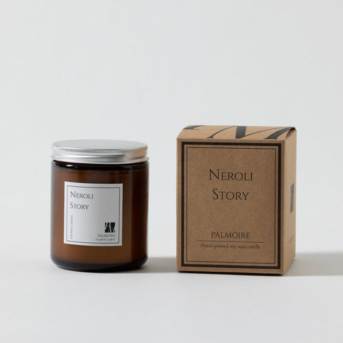 Amber glass soy wax candle with silver lid and white label beside a brown cardboard box labeled Neroli Story Palamour.