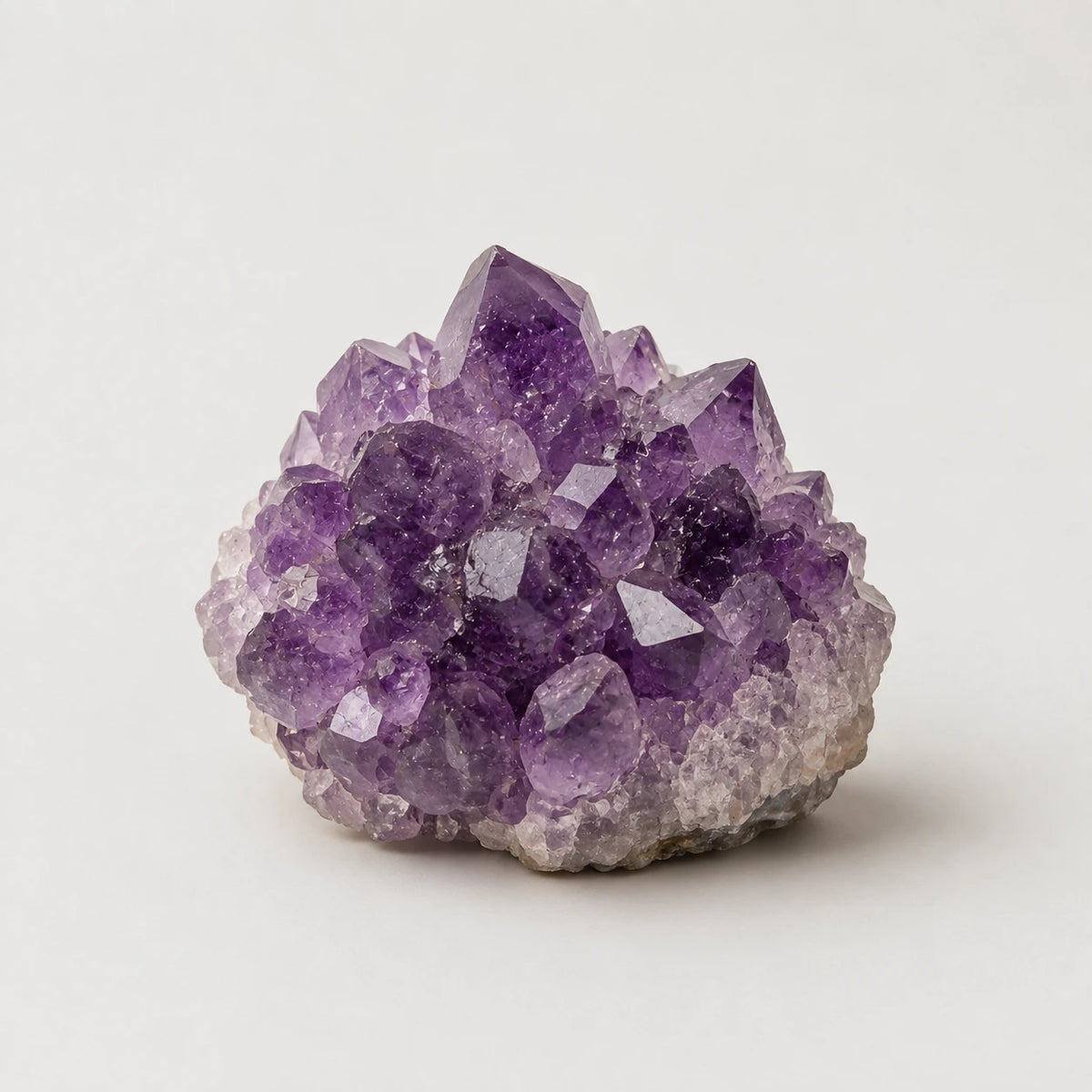 A natural amethyst crystal cluster with prominent purple and lavender crystalline points on a light gray matrix, photographed on a seamless light gray background.
