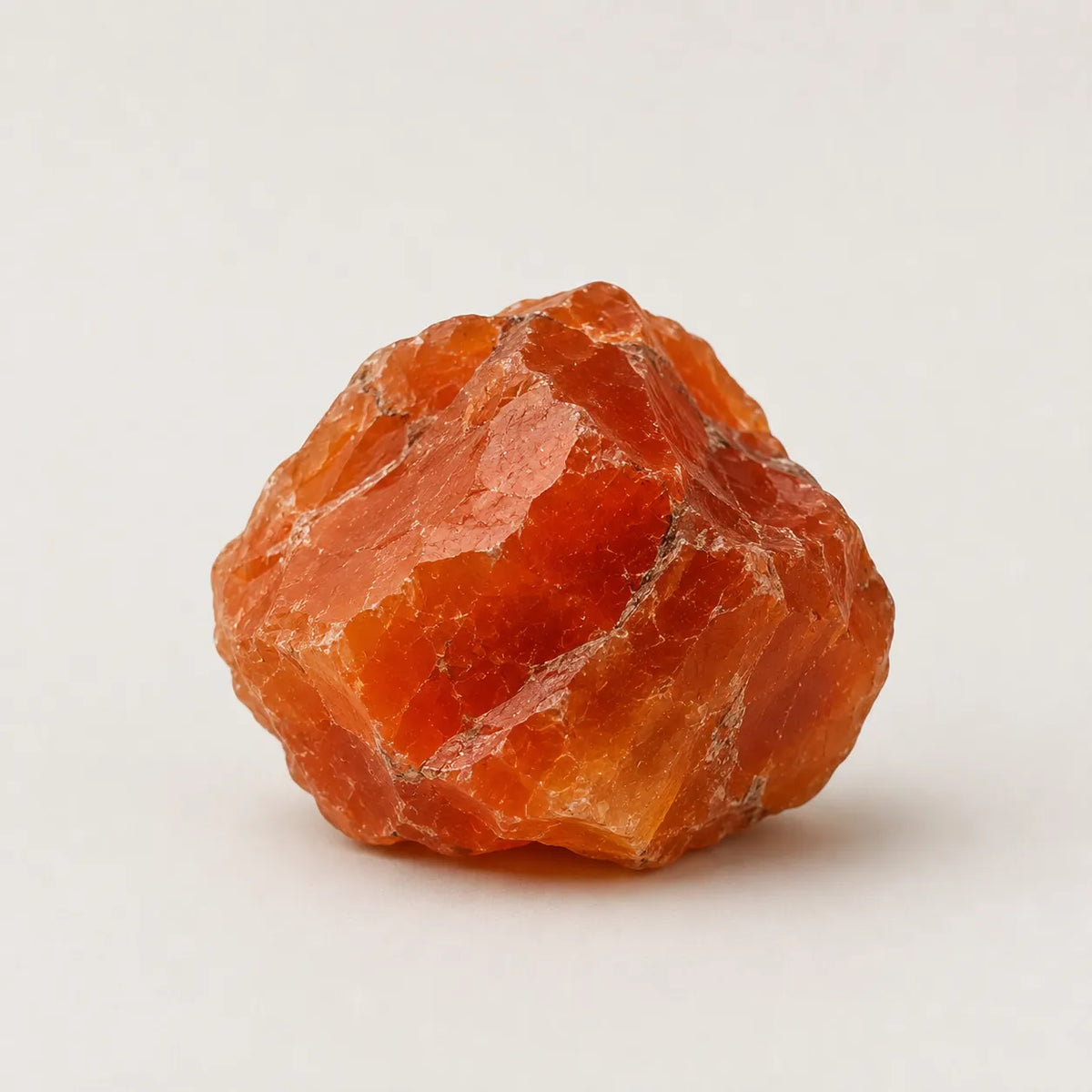A rough, unpolished piece of orange-red crystal, likely amethyst or quartz, photographed on a clean, light off-white background.