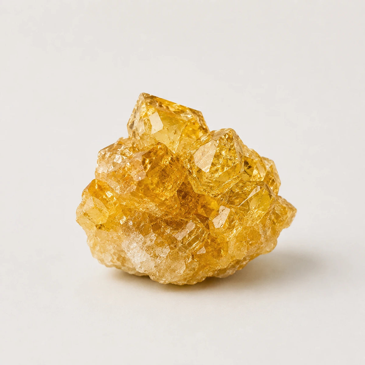 A cluster of yellow crystal sugar or quartz with rough, natural facets, photographed on a clean, light off-white background.