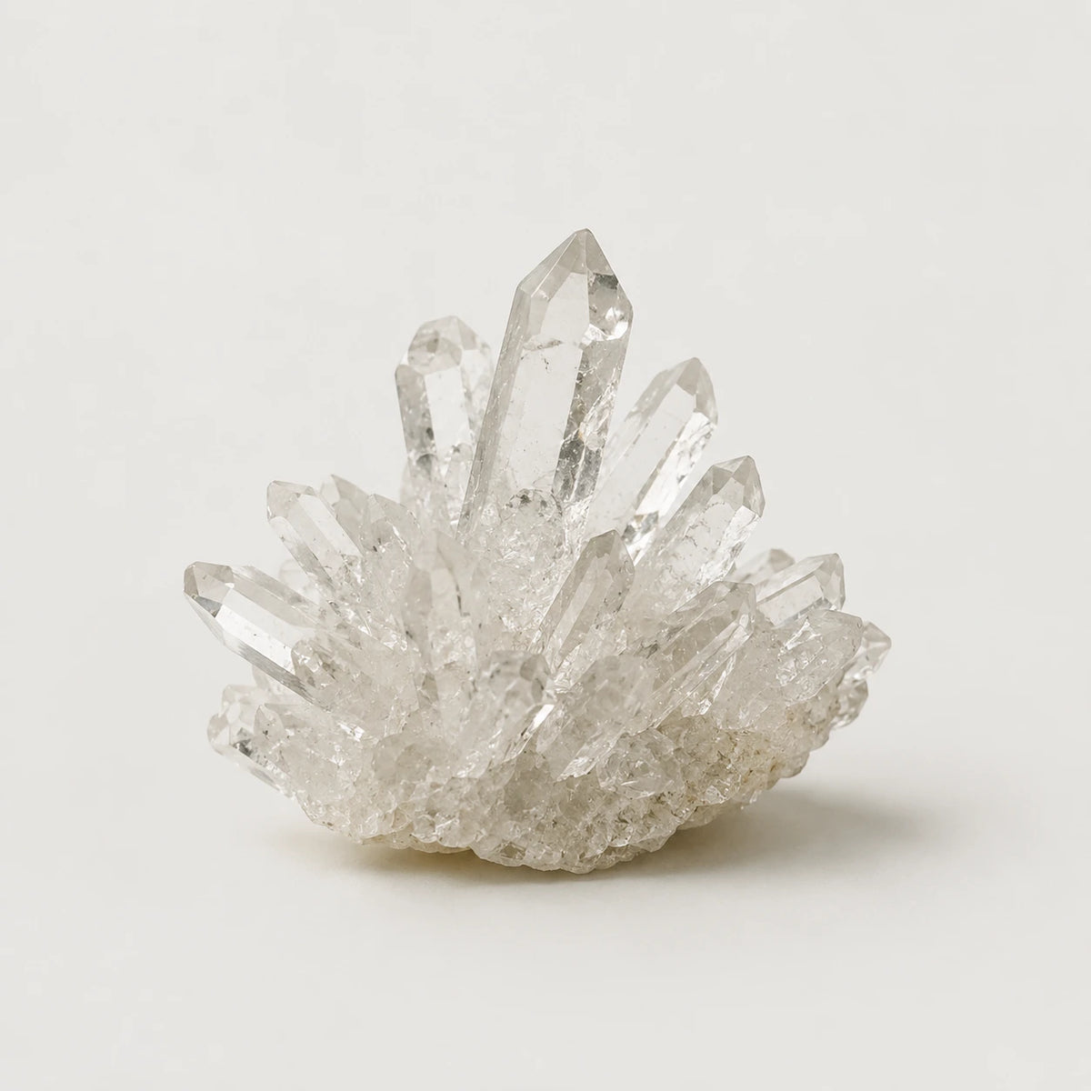 A cluster of clear quartz crystal points on a textured matrix, photographed against a neutral light gray background.