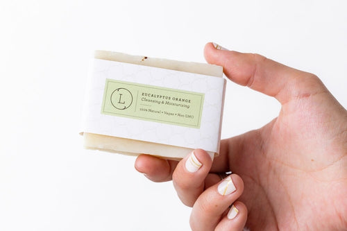 Hand holding rectangular eucalyptus natural handmade soap bar with green label and white wrapper.