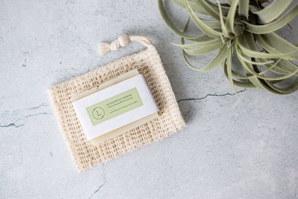 Rectangular eucalyptus natural handmade soap bar with light green label, resting on textured beige soap pouch on gray surface.