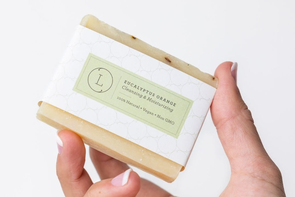 Handmade eucalyptus soap bar with green label and natural beige color held in hand.