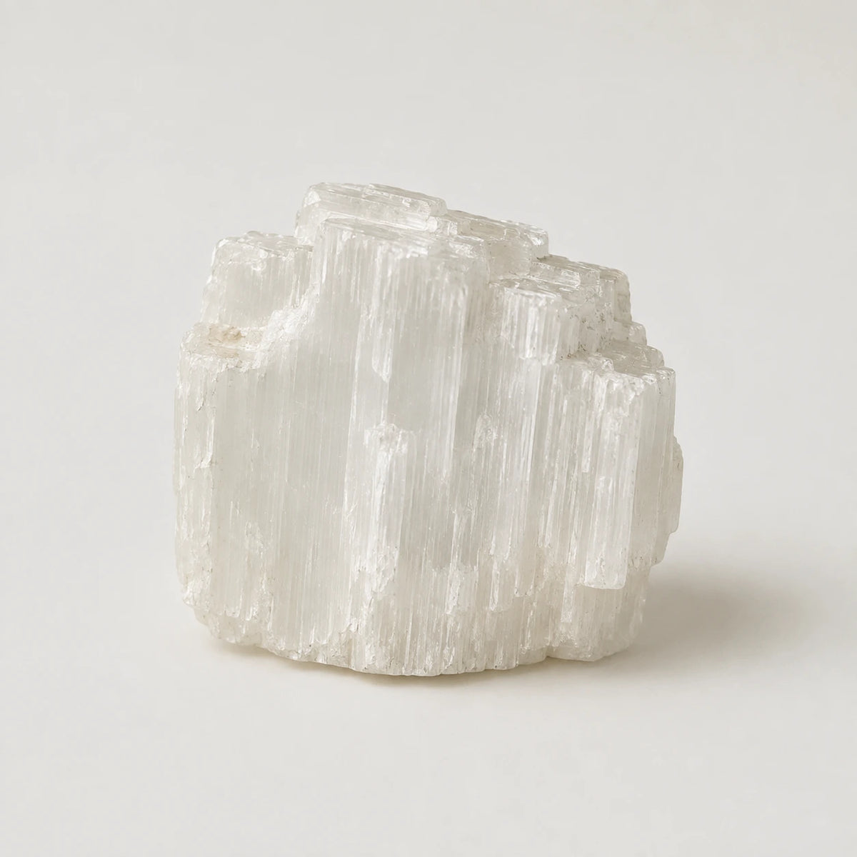 A natural translucent white crystal cluster with vertical striations, photographed on a clean light gray studio background.