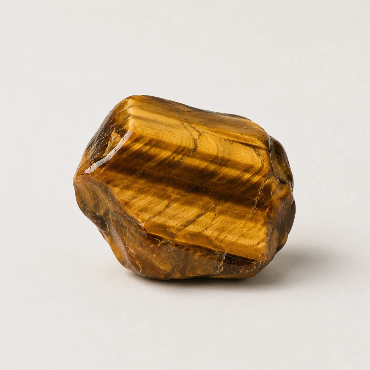 A polished tiger's eye stone with characteristic golden-brown bands, photographed on a clean, light gray background.