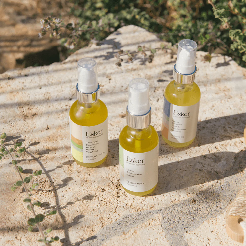 Three bottles of Esker botanical body oils placed on a stone surface outdoors to highlight restorative and natural skincare ingredients.