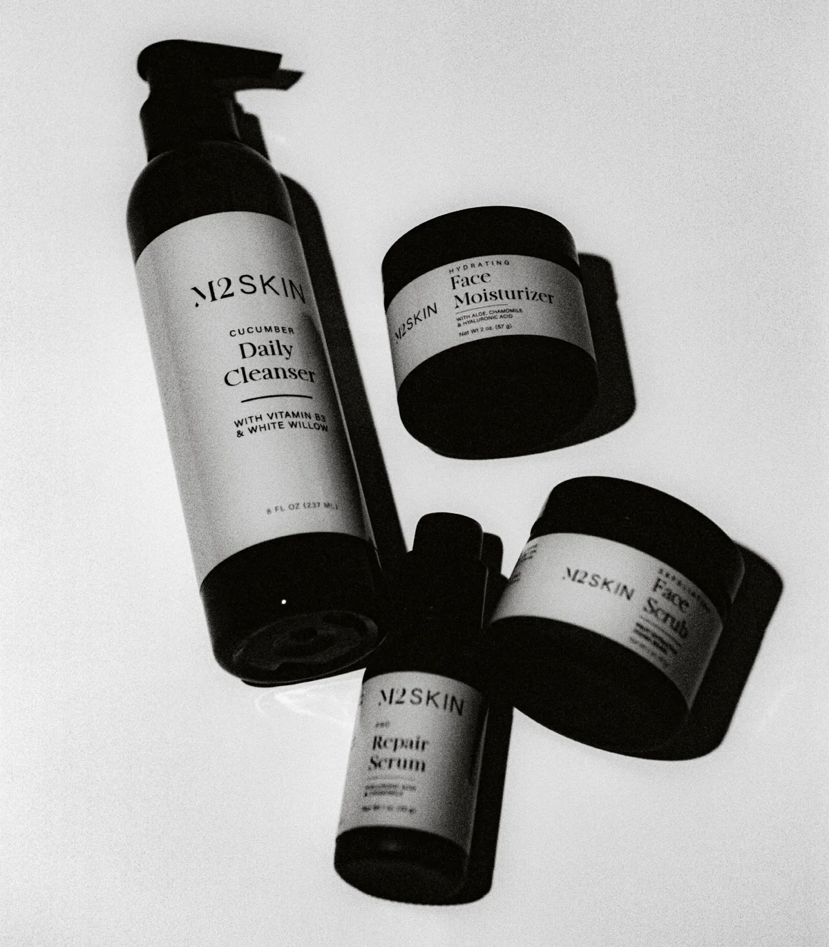 A monochrome collection of M2 SKIN products including cucumber daily cleanser, face moisturizer, repair serum, and face scrub for a complete skincare routine.