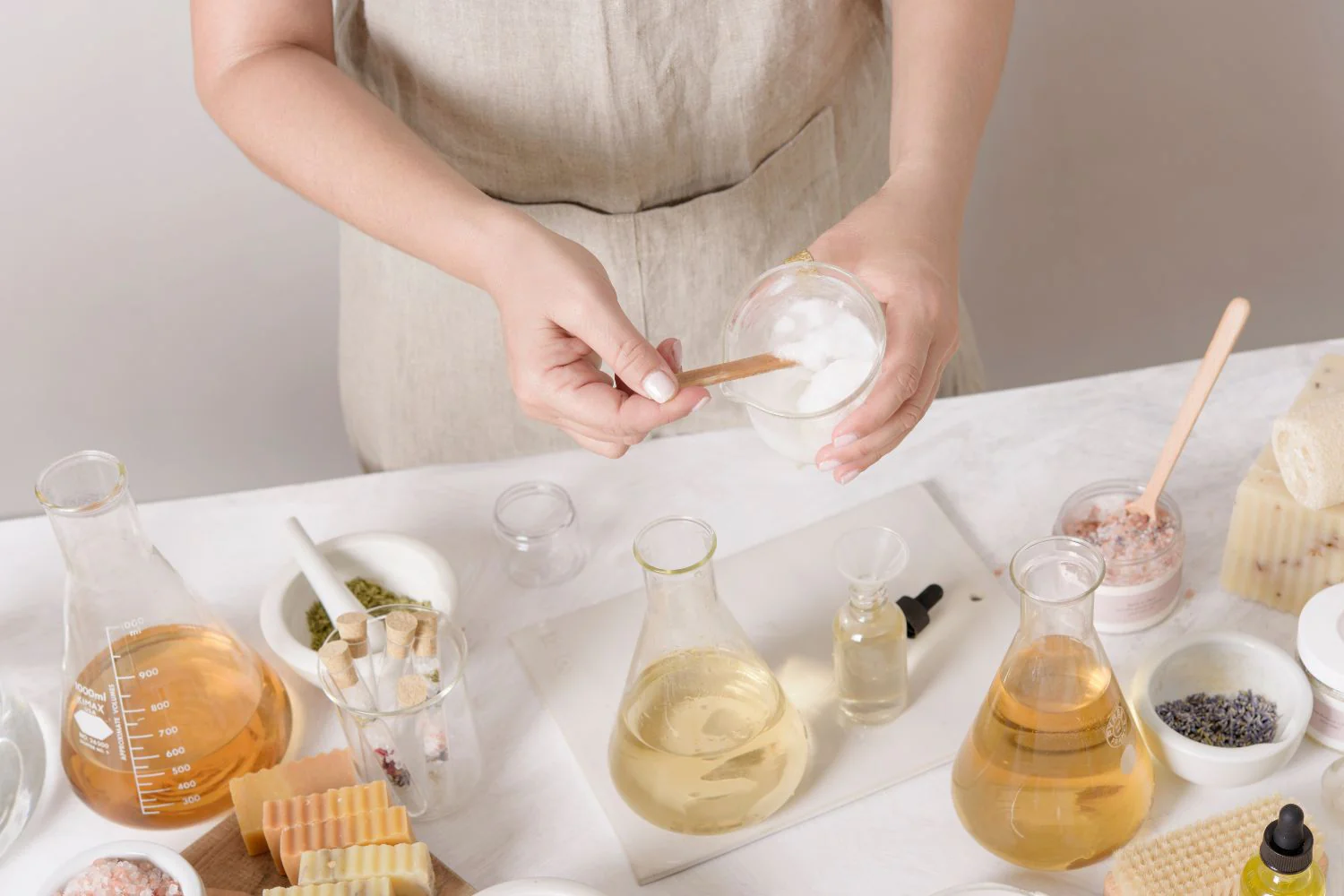 An artisan mixing natural ingredients in a lab setting with beakers of essential oils and botanical herbs to create organic handmade skincare products.