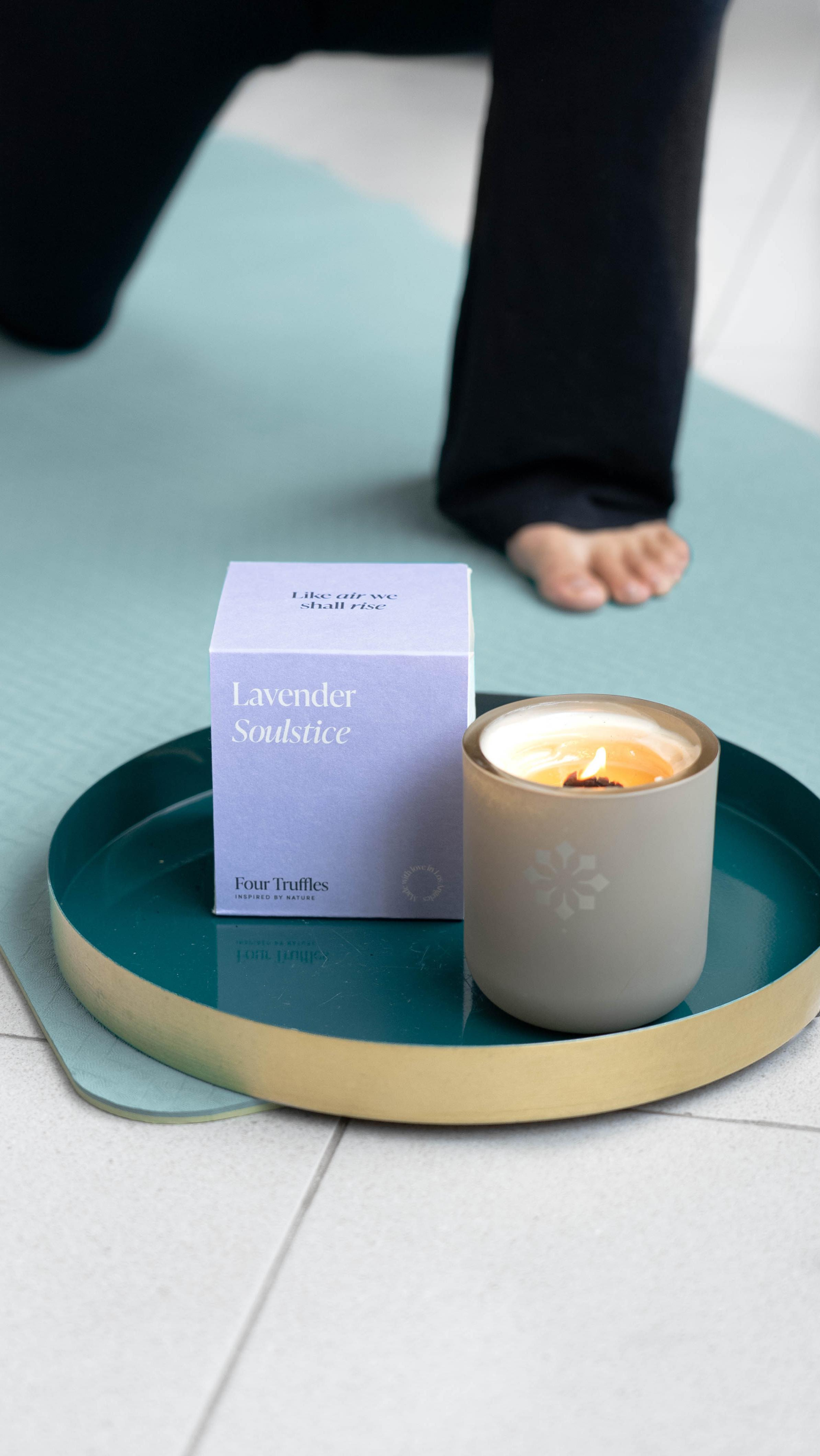 A lit Lavender Soulstice scented candle on a teal tray next to a yoga mat to create a peaceful atmosphere for mindfulness and meditation.