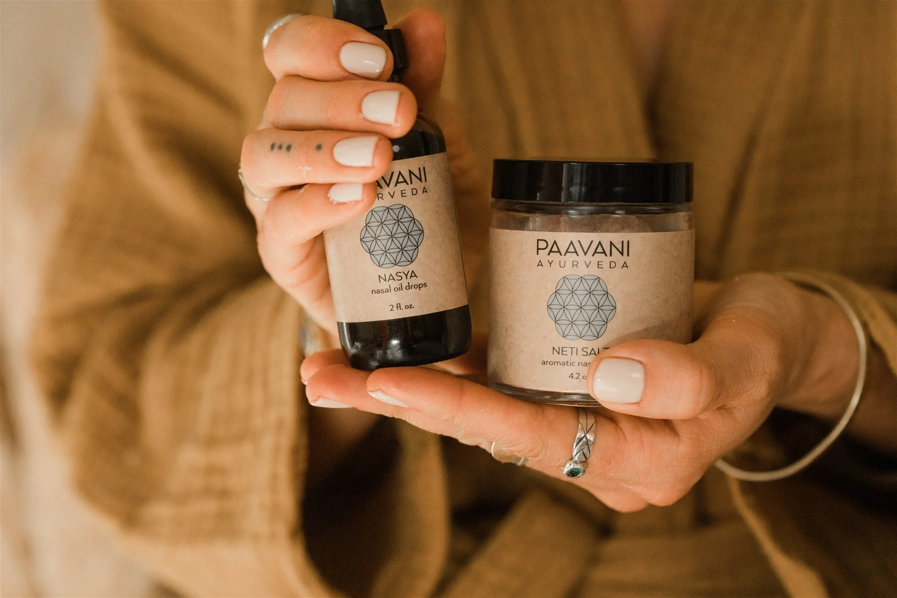 A person in a warm robe holds Paavani Ayurveda Nasya oil and Neti salt for a mindful daily sinus congestion relief ritual.