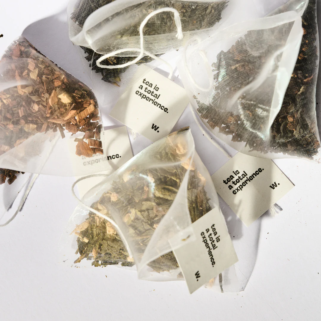 Close-up of pyramid organic herbal tea bags with "tea is a total experience" tags, showcasing loose leaf botanicals for a mindful wellness ritual.