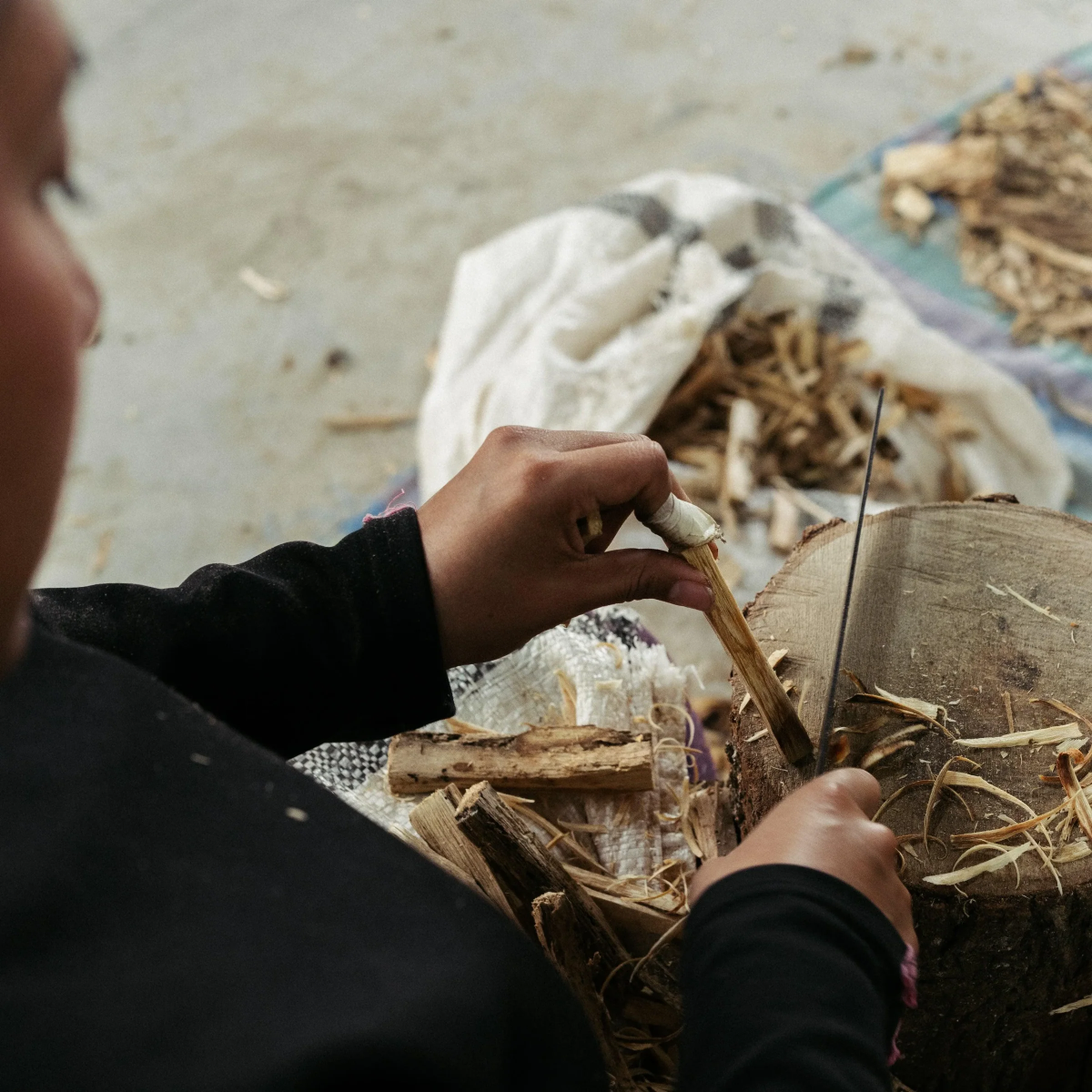 An artisan hand-carving natural Palo Santo wood sticks on a wooden block to ensure ethical sourcing for spiritual cleansing rituals.
