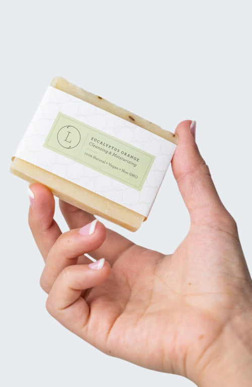 Hand holding rectangular eucalyptus natural handmade soap bar with white and green label.